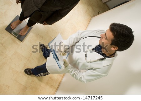 A young doctor, checks his patients weight on a scale. - horizontally framed
