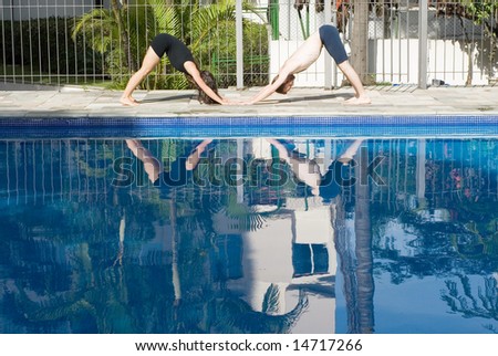 A man and a woman are exercising together beside a pool.  They are on the ground with torsos in the air.  They are looking away from camera.  Horizontally framed photo.