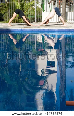 A man and a woman are exercising together beside a pool.  They are on the ground with torsos in the air.  They are looking away from camera.  Vertically framed photo.