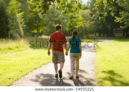 A couple walking through a park together. Rear view of them holding hands. Horizontally framed shot.