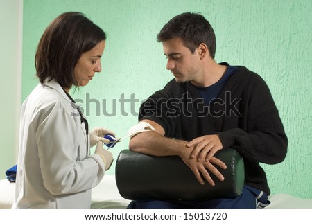 A female doctor, cuts the tape off the roll after applying it to a gauze pad on an arm. - horizontally framed
