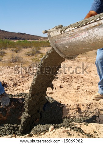 A cement truck is pouring cement into a hole in the desert.  Vertically framed shot.