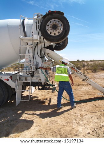 A man in the desert is working with a cement truck.  Vertically framed shot.