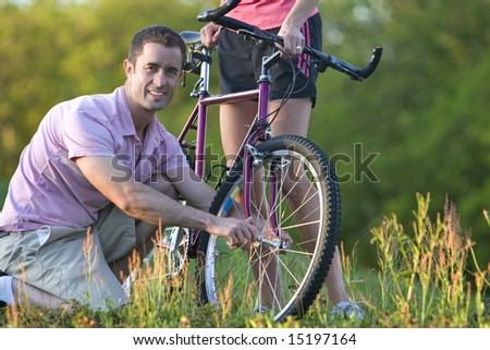 Close up of a man crouching down next to a bike smiling. Horizontally framed shot.