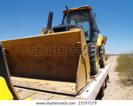 A work truck is hauling a steam shovel on a trailer.  Horizontally framed shot.