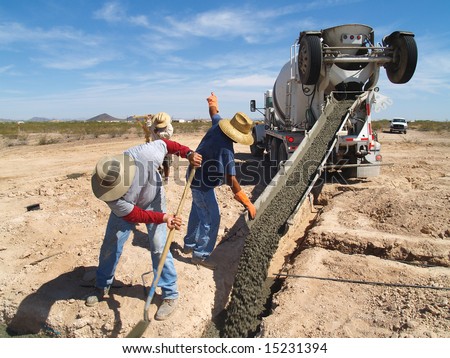 A cement truck is pouring cement into foundation.  A team of men are working together.  Horizontally framed shot.