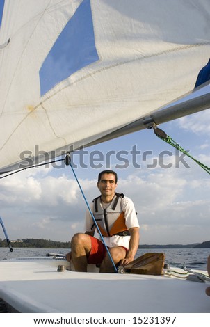 A young man is sitting in a sailboat.  He is smirking and looking away from the camera.  Vertically framed shot.