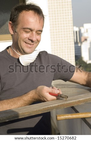 Man pulling nail with pliers. He is smiling and looking at the nail. He has a mask around his neck. Vertically framed shot.