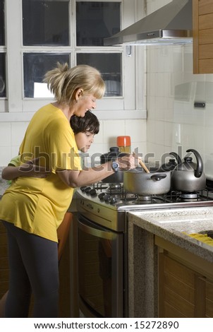 Boy standing next to woman with arm around waist. Boy watching woman stir pot on stove. Vertically framed photo.