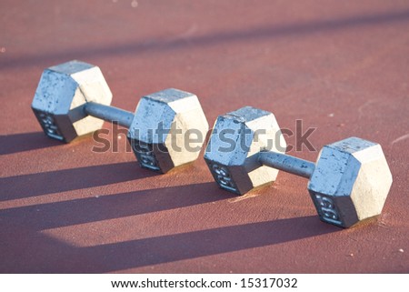 Two thirty-five pound hand weights are sitting side by side one another on a tennis court.  Horizontally framed shot.