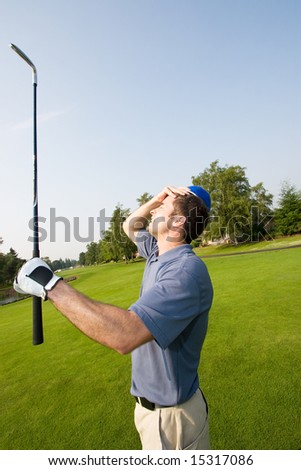 A man is grabbing his forehead in anger after missing a shot on a golf course.  He is holding a golf club and looking away from the camera.  Vertically framed shot.