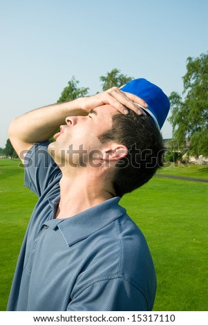 A man is grabbing his forehead in anger after missing a shot on a golf course.  He is looking away from the camera.  Vertically framed shot.
