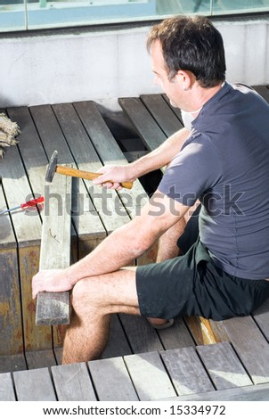 A man is about to pound a nail into a board with his hammer.  He is looking down at the nail.  Vertically framed shot.