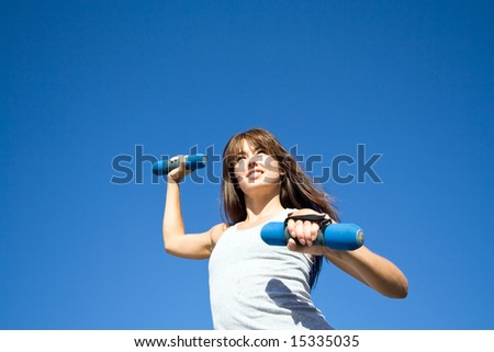 An attractive, fit woman is doing cardio with hand weights.  She is smiling and looking away from the camera.  Horizontally framed shot.