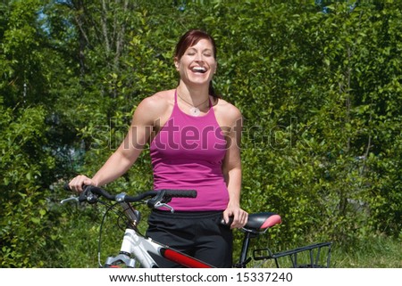 A woman on a sunny day, at a park, laughs by her bicycle. - horizontally framed