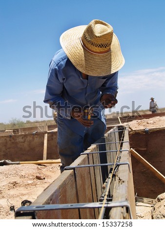 A construction worker is working on an excavation site.  He is bending down and looking at his work.  Vertically framed shot.