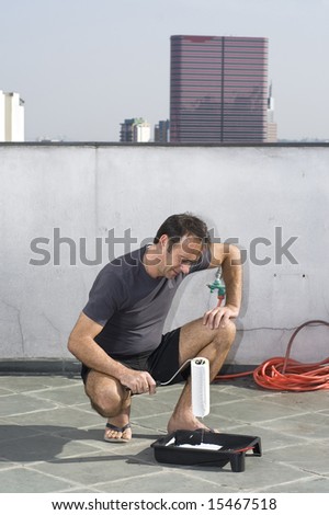 Smiling man squatting with hand on knee holding paint roller. He is looking at the paint roller. Vertically framed shot.