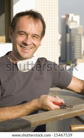 Man pulling nail with pliers. He is smiling and looking at the camera. He has a mask around his neck. Vertically framed shot.