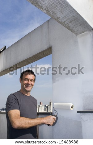 Man standing painting wall with paint roller. He is standing next to wall smiling at camera. Vertically framed shot.