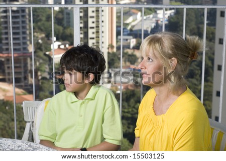 A mother and her child are seated at a table together.  The mother is holding a dog and they are both looking at something straight ahead.  Horizontally framed shot.