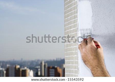 A man is holding a paintbrush and painting a wall white.  Horizontally framed shot.