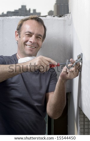 A man, installs a hook into a wall, while he sits smiling at the camera. Vertically framed shot.