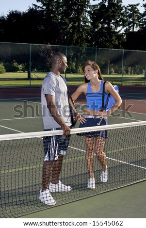 A young, active couple is standing on a tennis court.  They are wearing tennis clothes and smiling at each other.  Vertically framed photo.