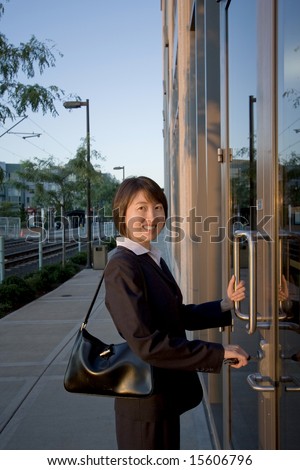A woman, standing in front of two large glass doors, smiling at the camera. Vertically framed shot.