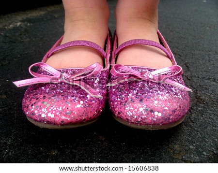 A little girl is wearing pink, sparkly tap shoes.  Horizontally framed shot.