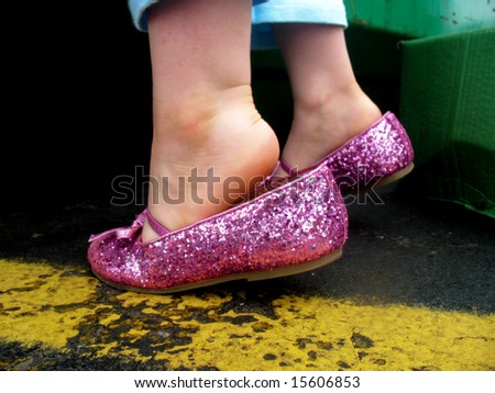 A little girl is wearing pink, sparkly tap shoes.  She is standing on her tiptoes.  Horizontally framed shot.