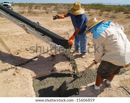 View of a cement truck\'s spout.  Men are directing the cement out of the spout.  Horizontally framed shot.