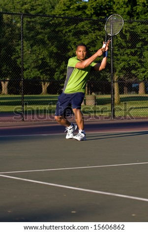 A man is outside on a tennis court playing tennis.  He is looking at the tennis ball.  Vertically framed shot.