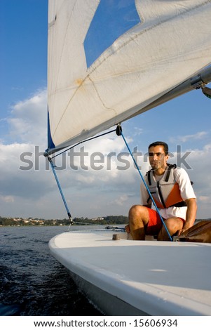 A young man is sitting in a sailboat.  He is smirking and looking away from the camera.  Vertically framed shot.