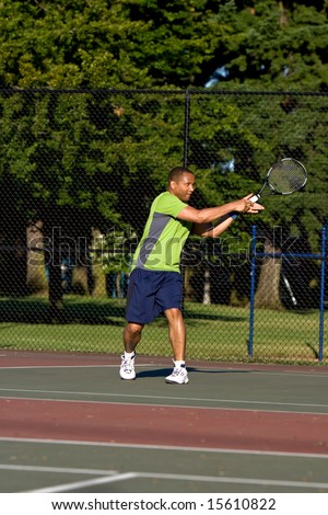 A man is outside on a tennis court playing tennis.  He just hit the ball and is looking away from the camera.  Vertically framed shot.
