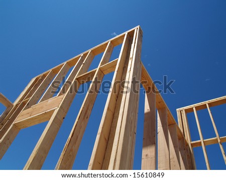 A house is being built on a construction site.  The walls have been put up and the frame can be seen.  Horizontally framed shot.