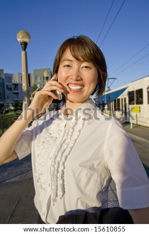 A woman, standing in front of the bus station, smiling in front of the camera. Using her cell phone. Vertically framed shot.