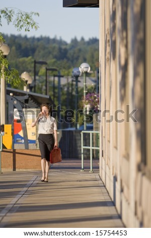 Young woman walks along building while talking on cell phone. Vertically framed photo.