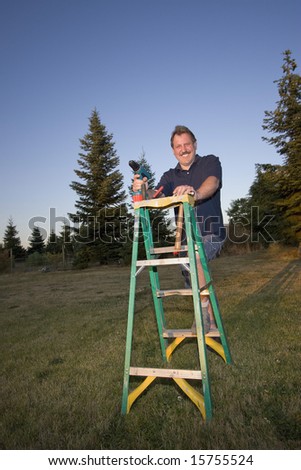 Man on ladder holding a drill and smiling. Vertically framed photograph