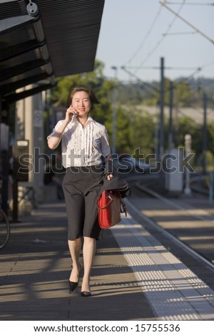 Young woman walks along tracks talking on her cell phone. She is carrying a red bag. Vertically framed photo.