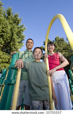 Smiling family stands on jungle gym looking at camera. Boy stands in front holding fireman\'s pole. Vertically framed photo.