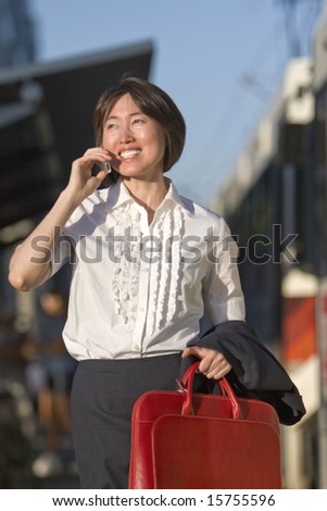 Young woman walks while talking on her cell phone. She is carrying a red bag. Vertically framed photo.
