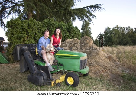 A man, woman and their dog sitting on a tractor smiling. Horizontally framed photograph
