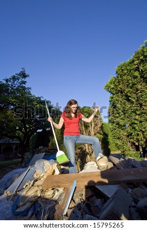Woman looking angry as she goes through a pile of garbage with a broom. Vertically framed photo.