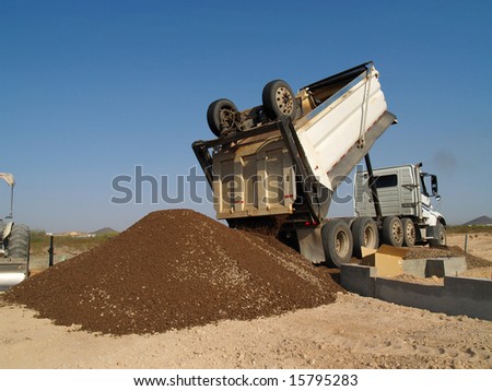Dump truck backed up to foundation dumping dirt. Horizontally framed shot.
