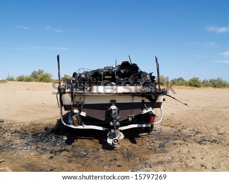 Burned wreckage of a power boat on a trailer. The boat is marooned in a desert, far from water. Horizontally framed shot.