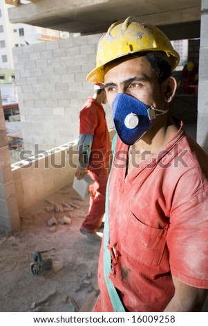 Construction worker stands in front of camera wearing blue dust mask. Vertically framed photo.