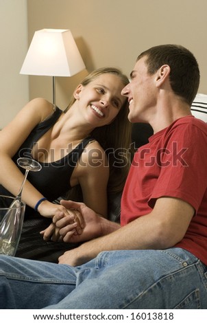 Man and woman relax on bed. A bucket of champagne is between them and they are holding hands. Horizontally framed photo.