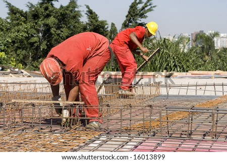 Construction workers in orange construction suit installs rebar. Horizontally framed photo.