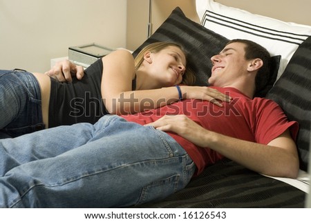 Man and woman relax on bed smiling at each other. Horizontally framed photo.