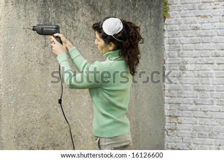 Woman with mask on head drills hole into wall with electric drill. Horizontally framed photo.
